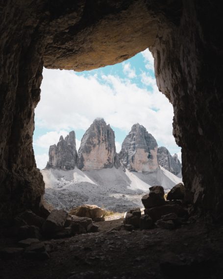 Uitzicht op bergtoppen vanuit een grot onder een blauwe lucht met wolken.