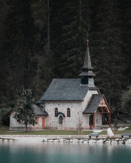 Klein stenen kerkje met toren aan een rustige, bosrijke waterkant.