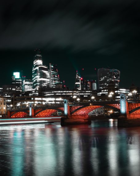 Stadse skyline bij nacht met verlichte brug en reflecties in het water.